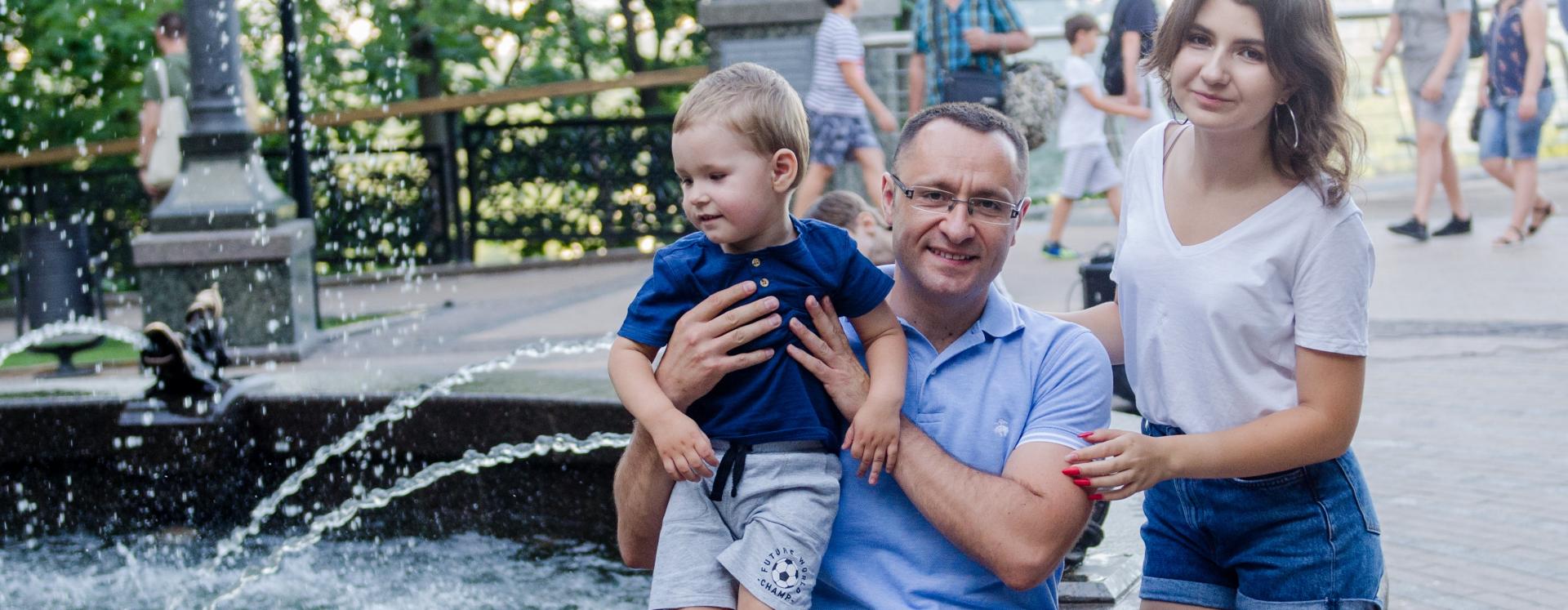 Vasyl Myroshnychenko Sitting By Fountain Holding Son In his Hands With Daughter Beside Him