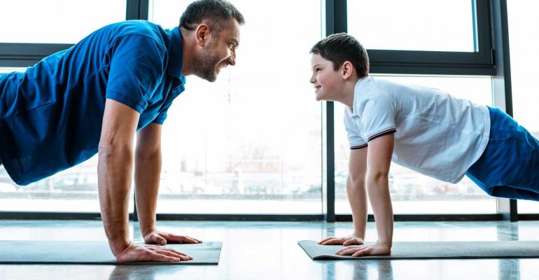 Grown Man And Teenage Boy Looking At Each Other While Doing Push-Ups
