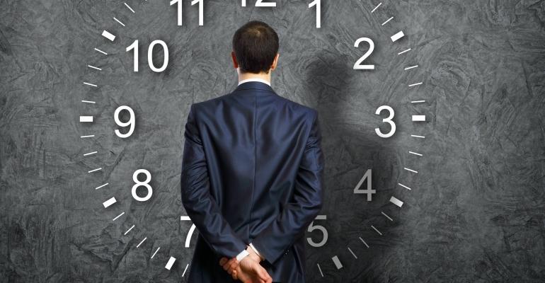 Man Looking At Giant Clock With His Back To Facing Us