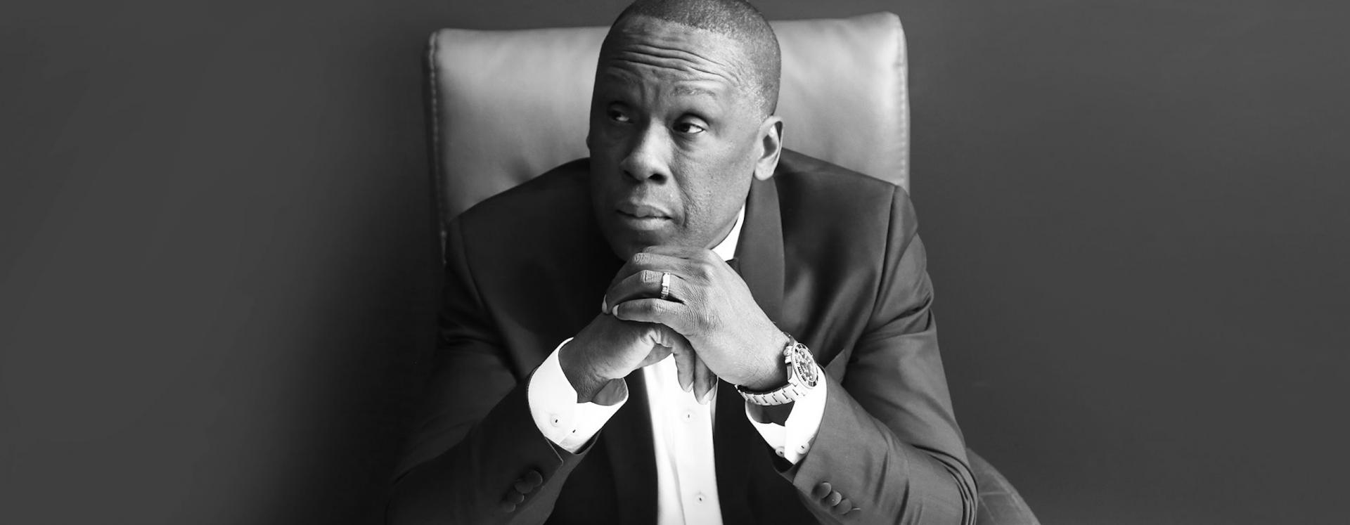 Black And White Photo Of Bruny Surin Sitting Down With Both Hands Under His Chin