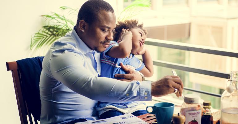 African American Dad Holding Young Child In Arms While Eating Food