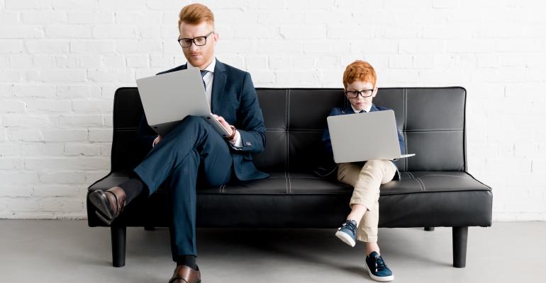 Business Man and Young Boy In Suit Sitting On Sofa With Their Laptops