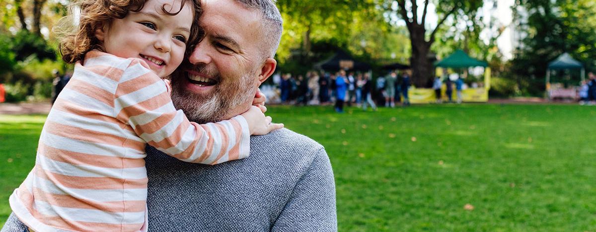 Middle Age Man Holding Young Child In Arms and Both Smiling