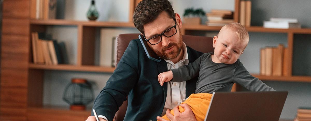 Busy Business Man On Telephone In Front of Computer Holding Baby