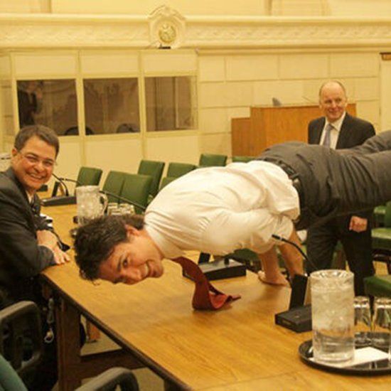 Justin Trudeau Smiling And Doing Yoga Pose On Table At Work In Front of Colleagues