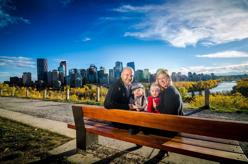 Kirk Bodnar Sitting On Park Bench With Family Overlooking City Of Calgary, Canada