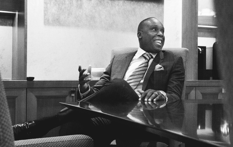 Bruny Surin Sitting At Desk In Business Suit And Smiling 