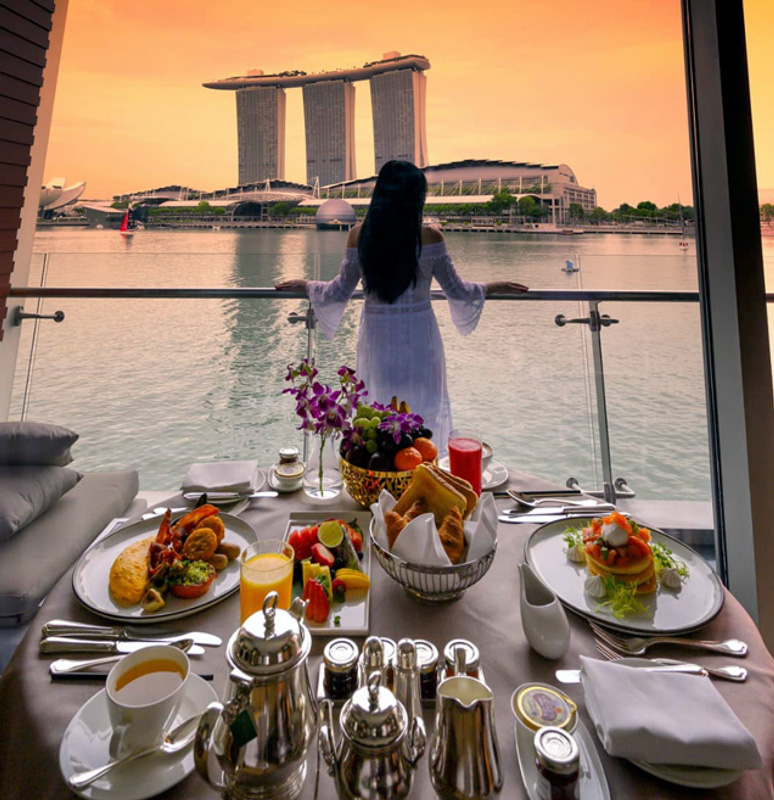 Woman Having Breakfast On Balcony Overlooking Marina Bay From her Hotel Room At The Fullerton Bay Hotel Singapore