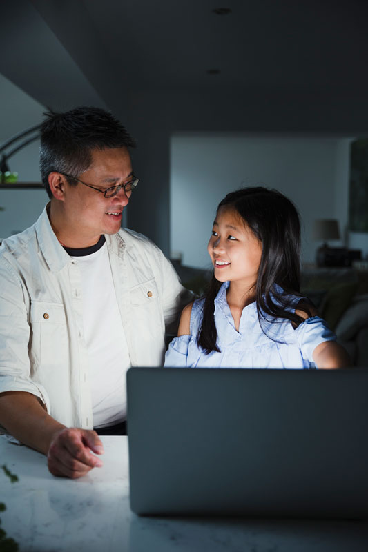 Smiling Asian Father Helping Young Daughter With A Computer 