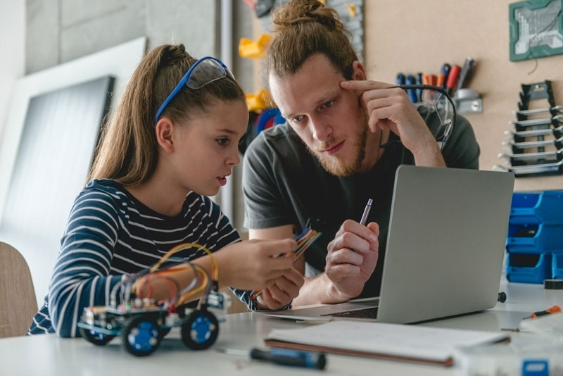 Father And Daughter Sitting In Front Of Computer Concentrating