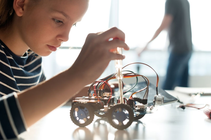 Teenage Girl With Screwdriver Making An Adjustment To A Small Robotic Vehicle