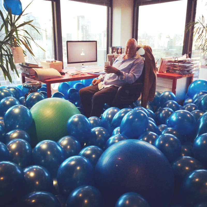 Frank Palmer Sitting In His Office Filled With Blue Balloons