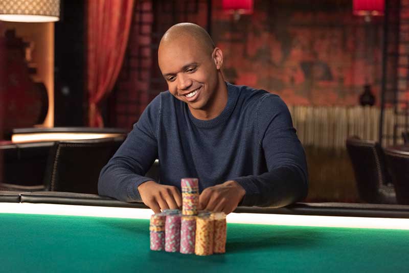 Poker Star Phil Ivey Sitting And Smiling At Poker Table With Poker Chips In Front Of Him