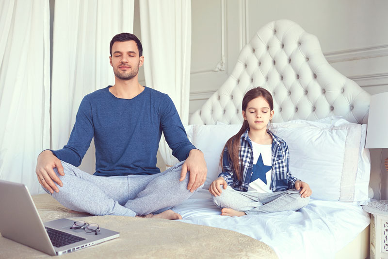 Father Daughter Sitting On Bed Meditating