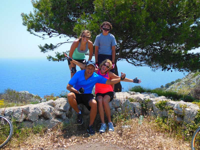 Oscar Munoz With Family Sitting On Rock Fence Overlooking Ocean Smiling And Waving  Cycling